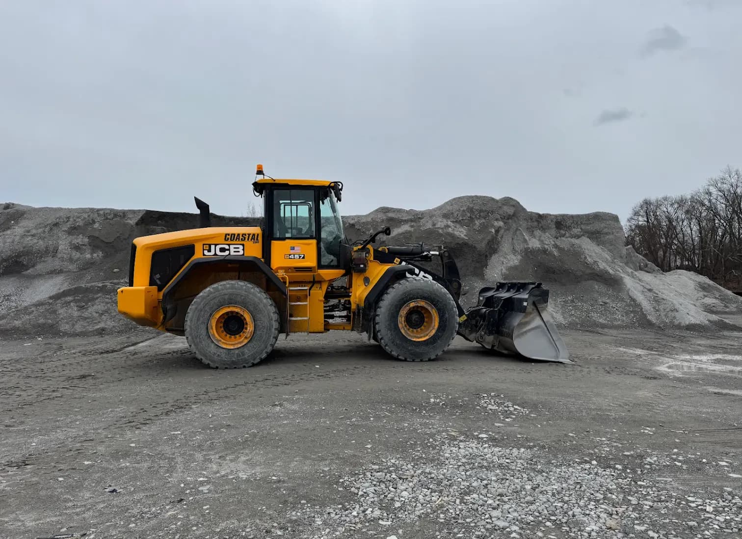 A Coastal Corp JCB 457 wheel loader with a high-capacity bucket, staged in front of large salt and sand stockpiles at the yard.